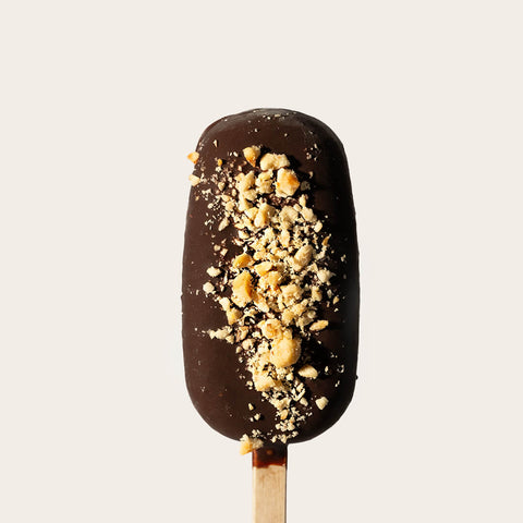 A hazelnut gelato bar coated in smooth dark chocolate, topped with crushed hazelnuts, on a plain light background. The bar is intact and looks perfectly fresh and indulgent.