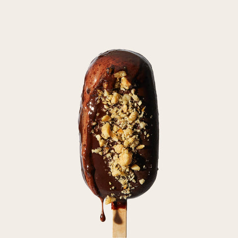 The same hazelnut gelato bar, now slightly melting, with rich chocolate drips adding texture and warmth. The hazelnut topping remains visible and appealing.