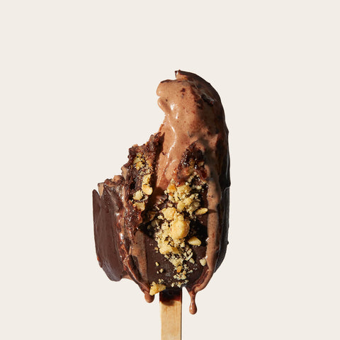 A bitten hazelnut gelato bar revealing its creamy interior, surrounded by a layer of dark chocolate and a scattering of hazelnuts. The melting chocolate adds a sense of indulgence.