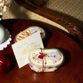 A cozy scene of two artisanal Nonna Lia tiramisu desserts, accompanied by the holiday card, placed on a polished wooden table with festive accents like a red ornament and warm lighting. It conveys elegance and holiday cheer, ideal for gift-giving moments.